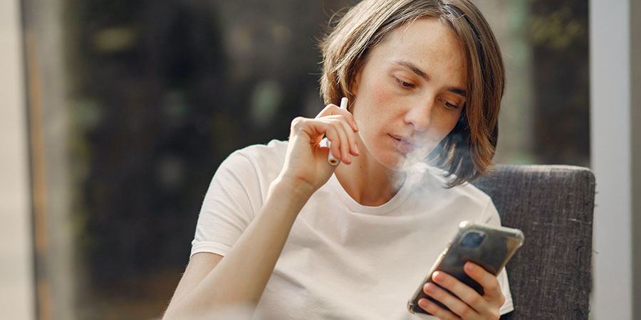 woman with blonde dark brown hair wearing white tshirt, sitting, smoking and using her mobile phone